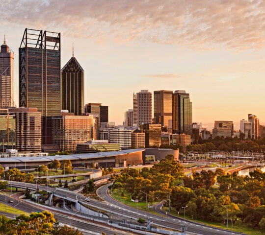 Western Australia capital city Perth at sunrise during golden hour. Bright warm sun light sheds on skyscrapers and city-line.
