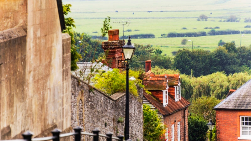 Traditional red brick houses and a street lamp on a hill overlooking green countryside.
