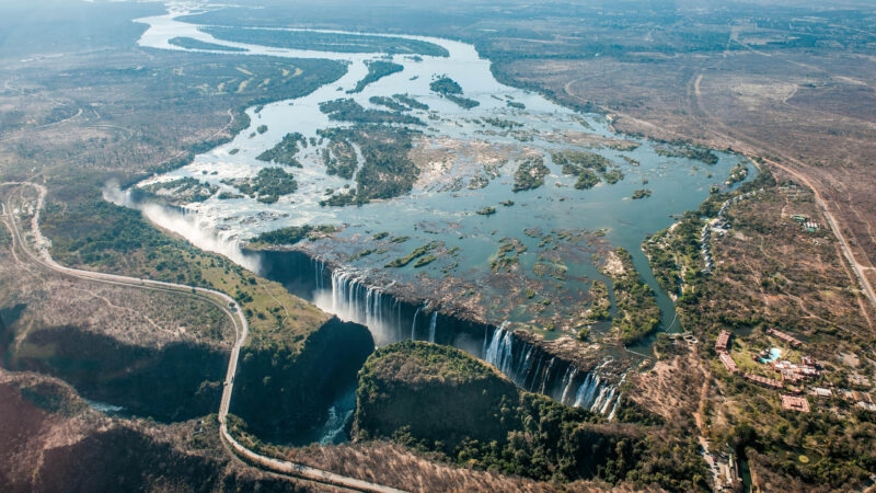 High-angle aerial view of the wide Zambezi River plunging over the edge of the large Victoria Falls waterfall.