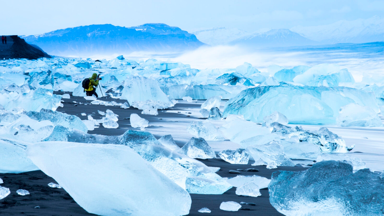 Traveller photographing broken ice which has washed up on the shore of Jokulsarlon Ice Beach, Iceland