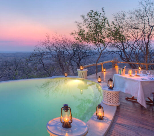 Private dining at Ikuka Safari Camp, featuring an intimate table set up for two next to a swimming pool surrounded by lanterns.