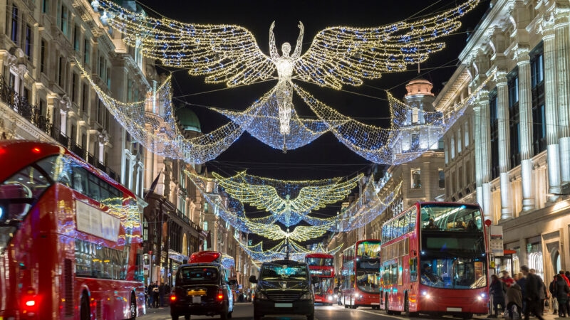 Red double-decker buses pass under twinkling Christmas lights al