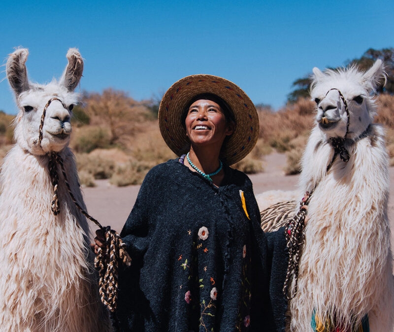 A woman smiling between two llamas under a clear blue sky on luxury Chile tours.