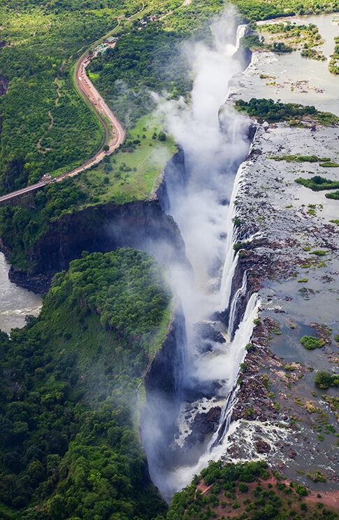 Aerial view of Victoria Falls, with water plunging into a deep, misty gorge next to lush green cliffs.