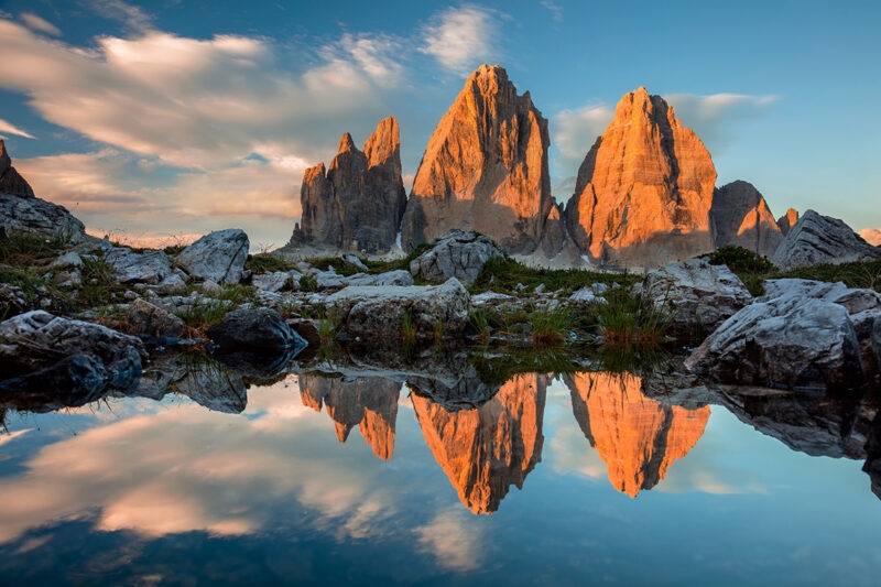 Luxury Italy Tours Three jagged mountain peaks at sunset reflected in the clear water of a small mountain lake.