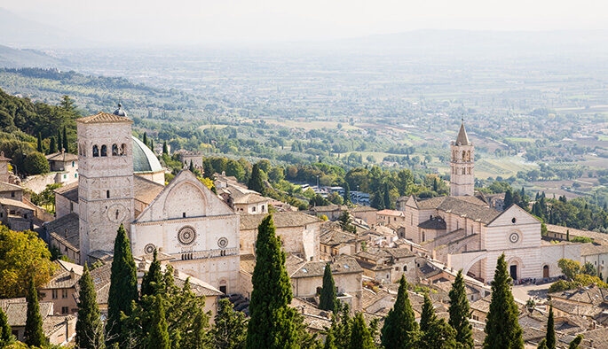 Luxury Italy Tours - A view from above the town of Assisi in Umbria, Italy, a traditional hilltop town with a church and cathedral, pale stone buildings and a view of a green valley
