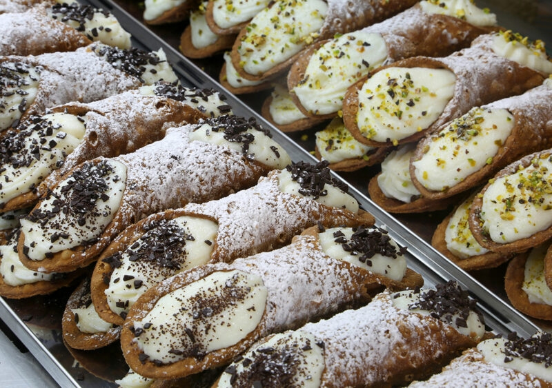 Luxury Italy Tours - Rows of typical Sicilian cannoli, a crisp pastry cylinder stuffed with ricotta cheese and sprinkled with powered sugar, nuts, and chocolate shavings