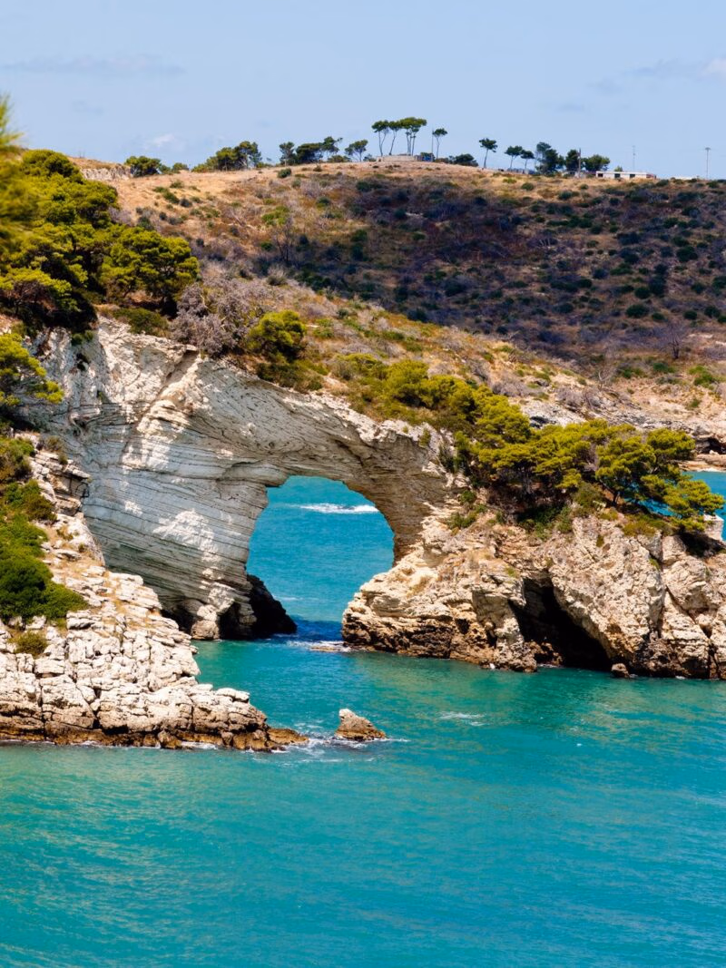 Luxury Italy Tours - Gargano national park in Puglia, Italy, with a dramatic rock archway eroded out of the coastline through which bright blue sea is visible