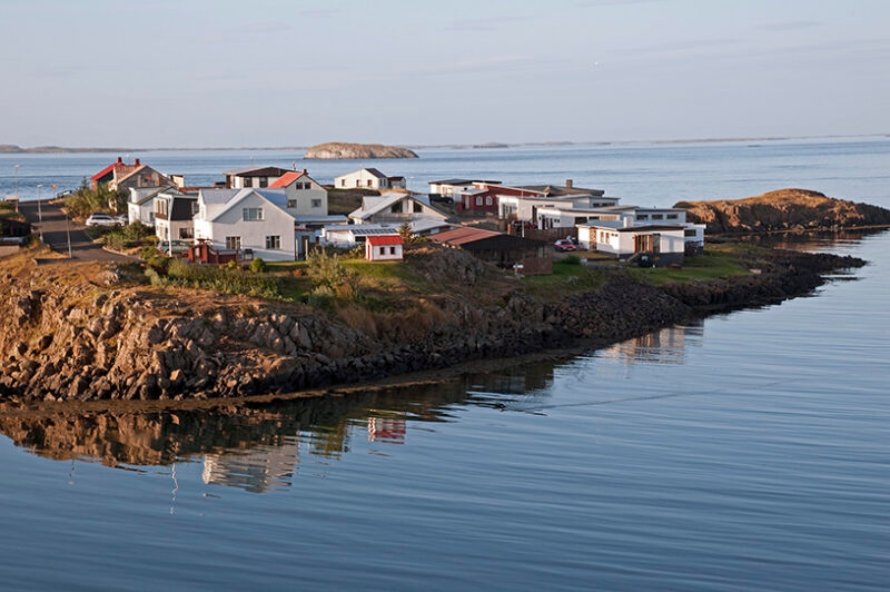 Small white and colorful houses stand on a rocky peninsula surrounded by calm, reflecting water, ideal for luxury Iceland holidays.