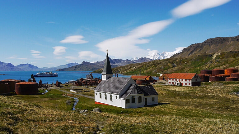 Wide view of the historic white church and rusty oil tanks at the Grytviken whaling station in South Georgia.