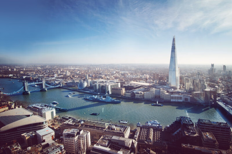 Aerial view of London featuring the River Thames, the Shard skyscraper, and the historic Tower Bridge.