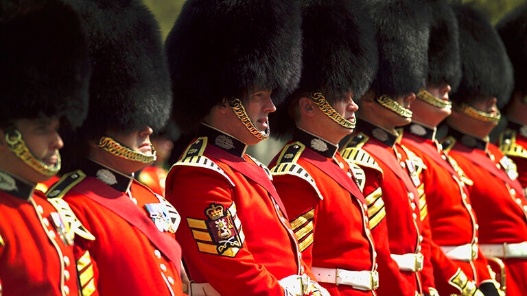 British Foot Guards in red tunics and tall black bearskin hats standing in a close, military formation.