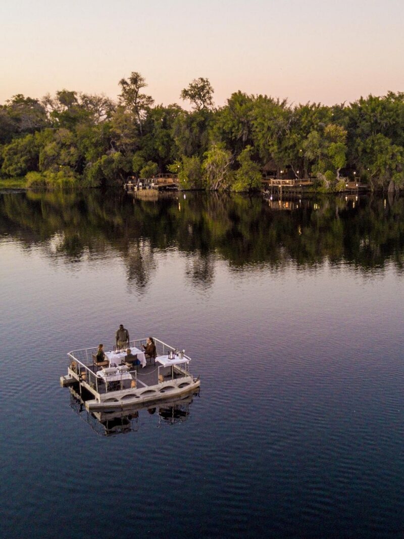 An aerial view of people dining on a small floating deck in a river during twilight.