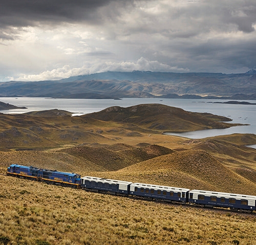 A train traveling through hills past a lake on luxury Peru train journeys.