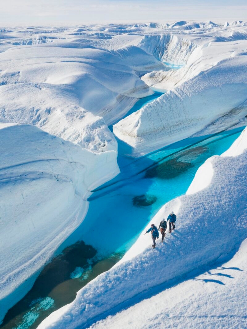 Aerial view of hikers on snow ridges by turquoise water, featured on luxury Polar trips.