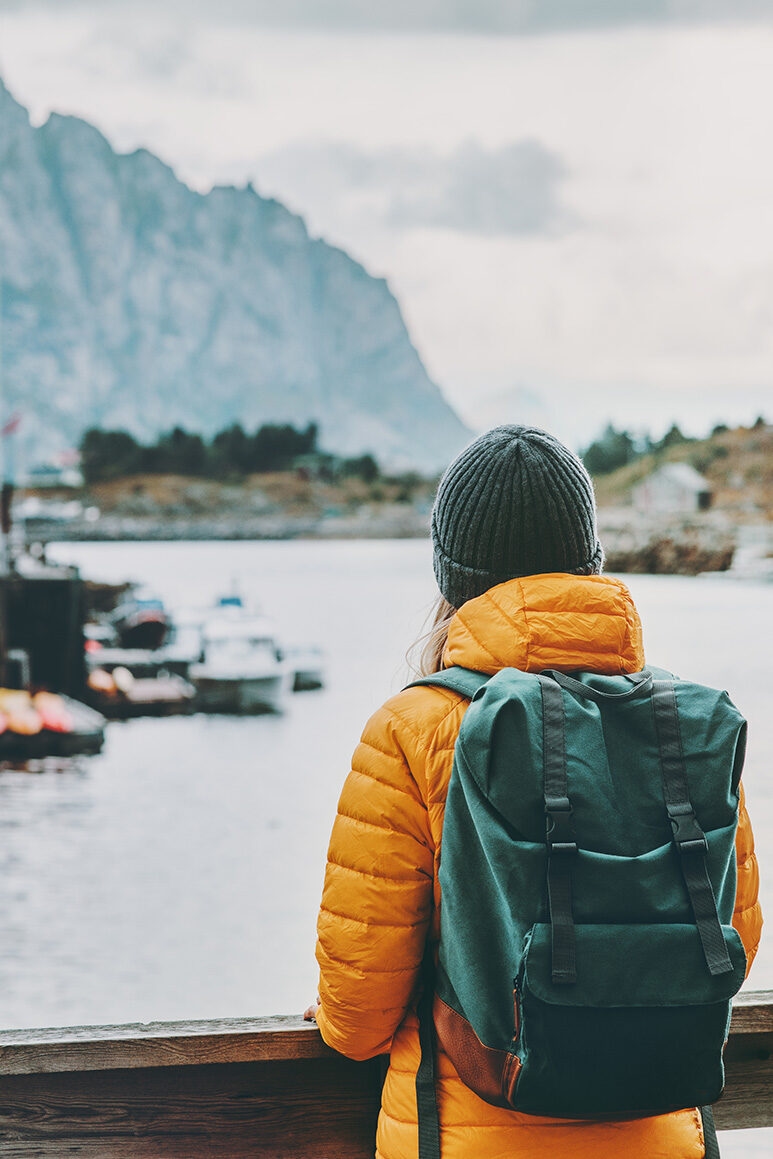 A hiker in an orange jacket viewing an Arctic harbor, a scene from luxury Polar vacations.