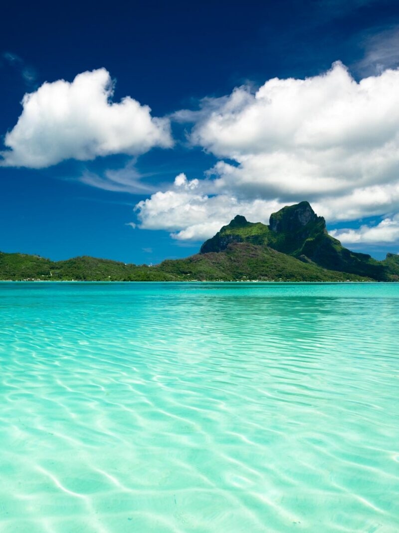 Volcanic mountain peak overlooking a clear turquoise lagoon during luxury South Pacific vacations.
