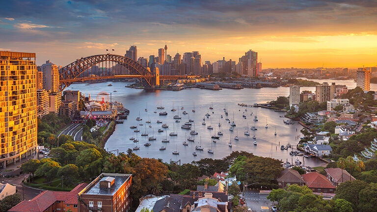 Sunset over Sydney Harbour with boats and the city skyline for luxury Australasia vacations.