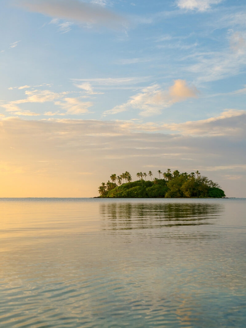A remote tropical island surrounded by calm water at sunset on luxury Australasia tours.