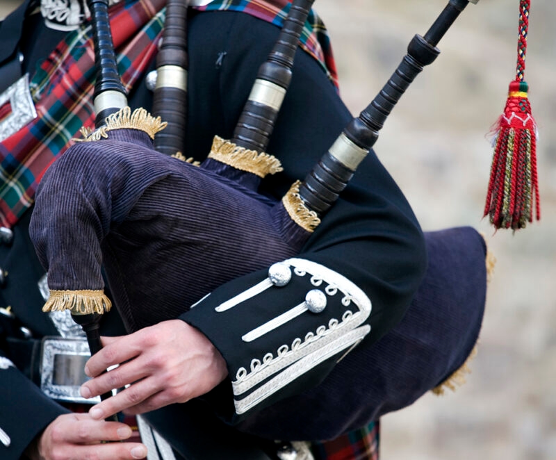 Close-up of a person in tartan holding and playing the bagpipes, with gold and silver trim visible. Experience this on luxury Scotland vacations.