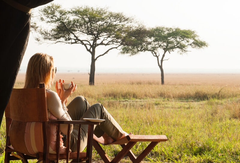 A woman sitting in a wooden chair watching the sunset during luxury Serengeti National Park tours.