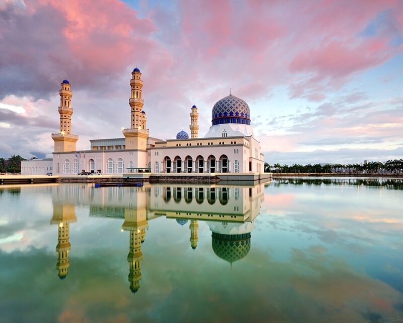 A beautiful white mosque with blue domes reflected in calm water during luxury Borneo holidays.