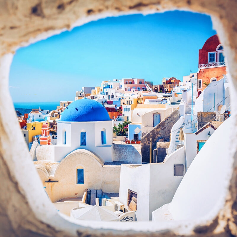 The bright white buildings and famous blue-domed churches of Santorini, Greece, overlooking the deep blue Aegean Sea and volcanic caldera.