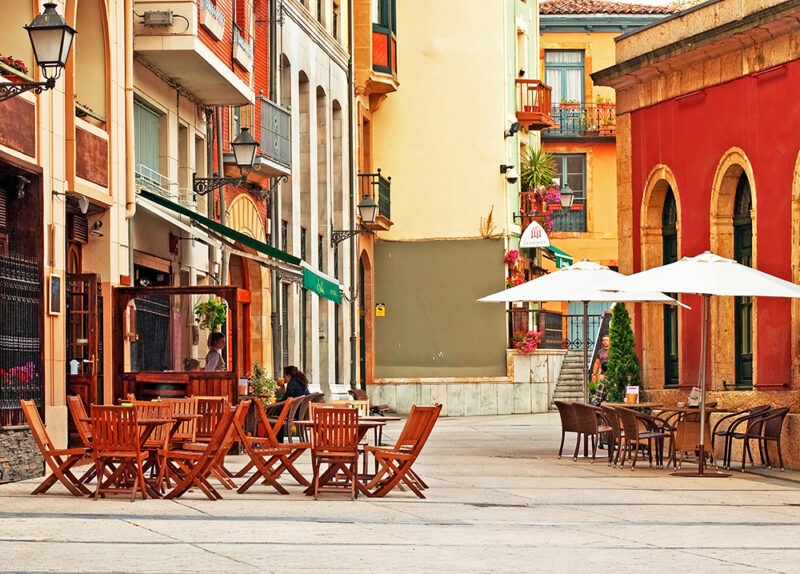 Empty cafe tables on a sunlit street with colorful buildings during luxury Portugal holidays.