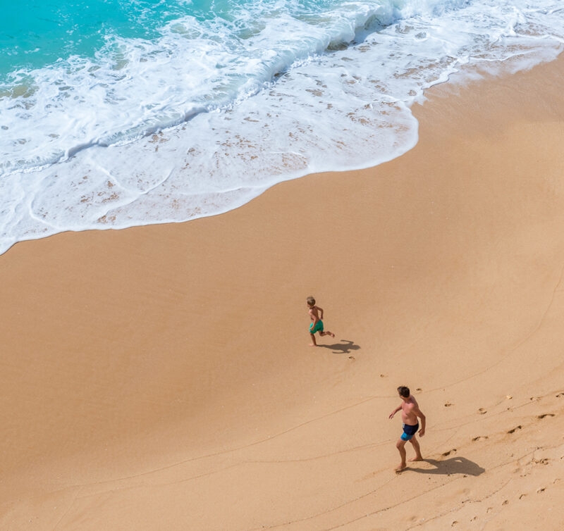 A father and his child running along a golden sand beach, Carvalho of Algarve, Portugal