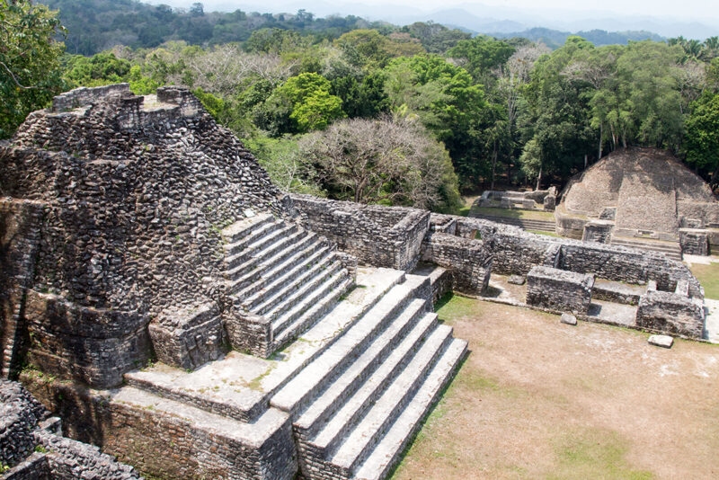 Ancient stone pyramid ruins and courtyards nestled within a thick green tropical forest.