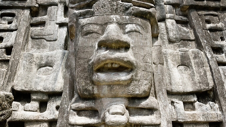 Close-up of an ancient stone face carving with detailed features on a weathered wall.