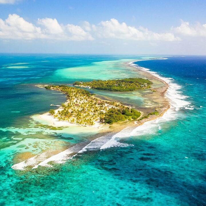 Aerial shot of a lush tropical island with white sand and palm trees surrounded by clear turquoise sea.