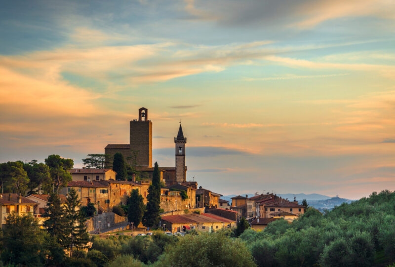 Sunset view of a medieval Italian village with stone towers and surrounding olive groves for luxury Tuscany vacations.