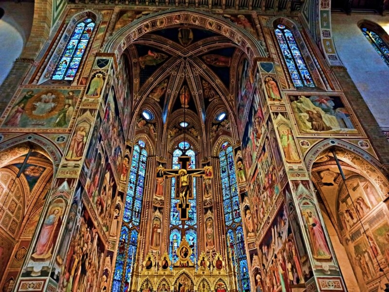 The interior of a grand cathedral with colorful frescoes and a large crucifix for luxury Tuscany tours.