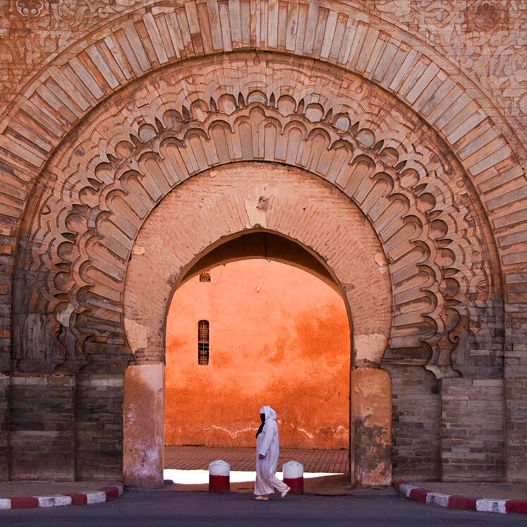 A person in white clothing walking under a large arched stone doorway