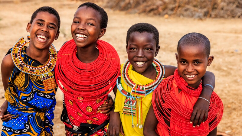 Smiling children wearing intricate traditional beaded necklaces during luxury Maasai Mara holidays.