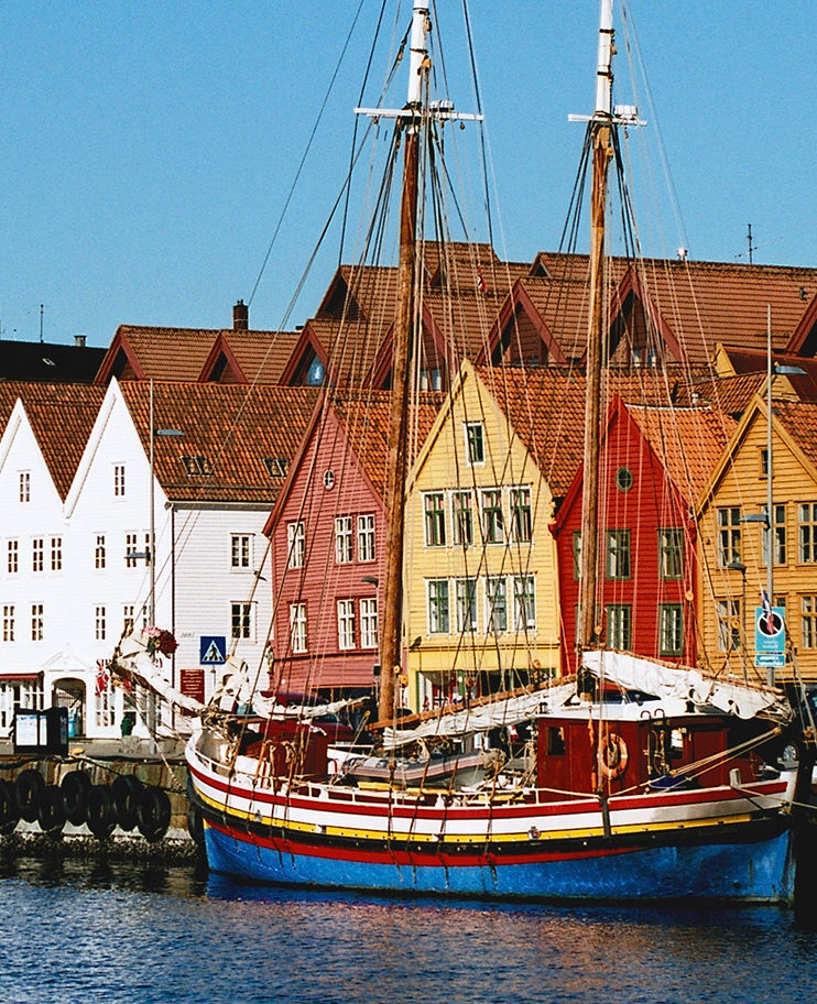 Old fishing buildings by the harbour in Bergen, Norway, with a tall mast ship docked next to them