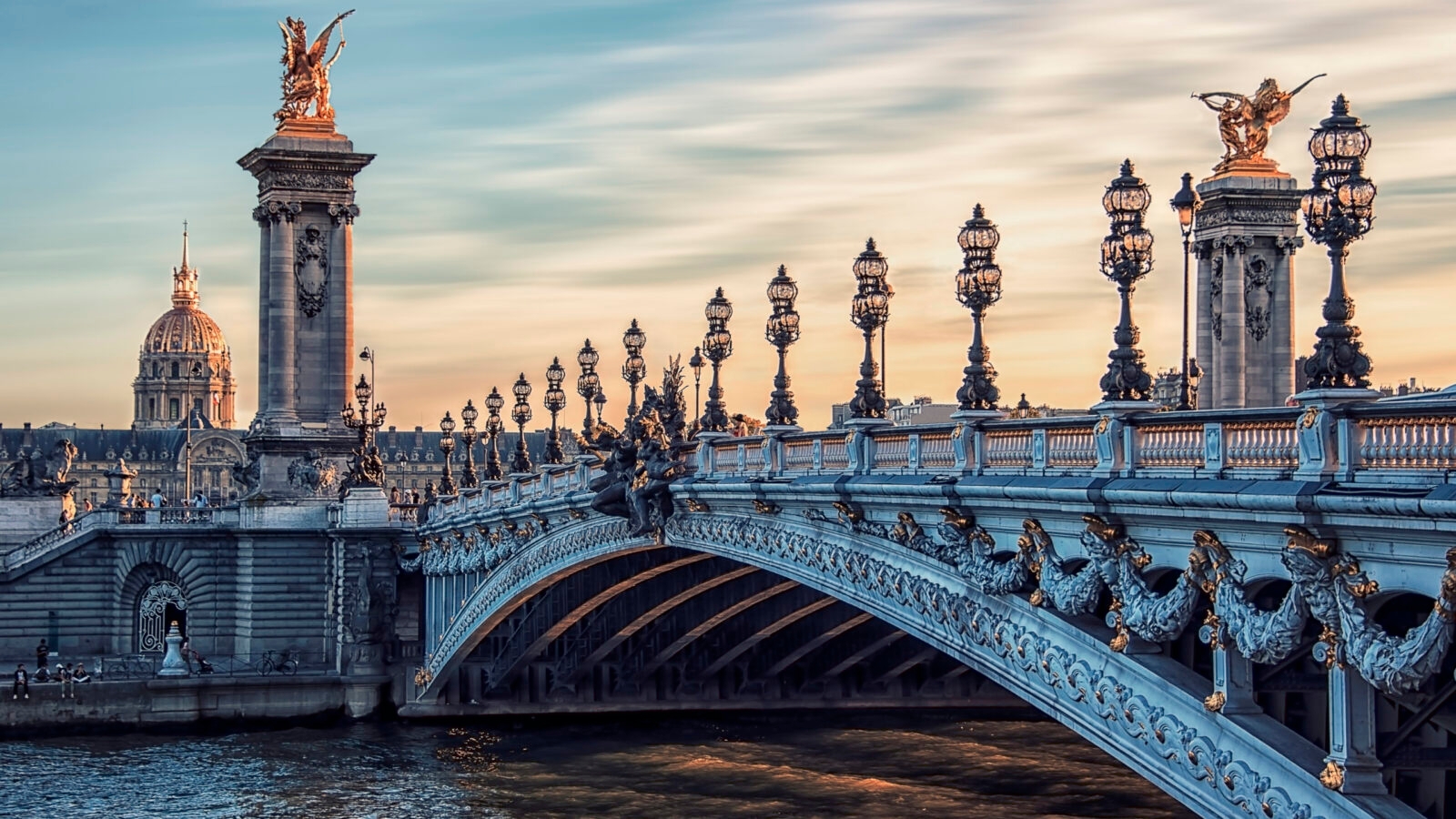 Luxury Grand Tours of Europe - Alexandre III bridge in Paris, a grand and ornate arched bridge over the River Seine with gothic black lampposts, and gold detailed statues on plinths