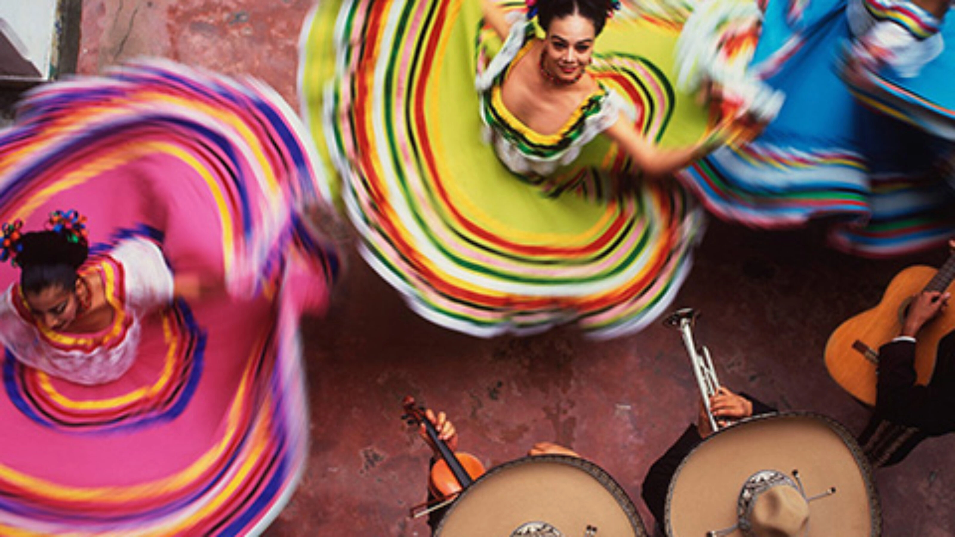 Overhead shot of dancers in colourful dresses with striped skirts twirling on a pink floor