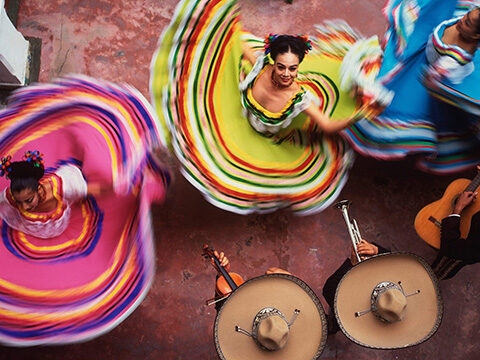 Overhead shot of dancers in colourful dresses with striped skirts twirling on a pink floor