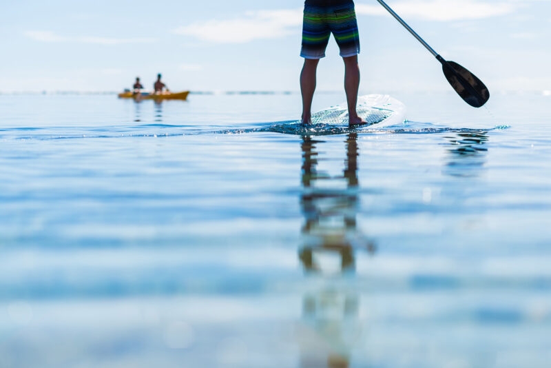 Close up of a person's legs as they stand on a paddle board in calm water