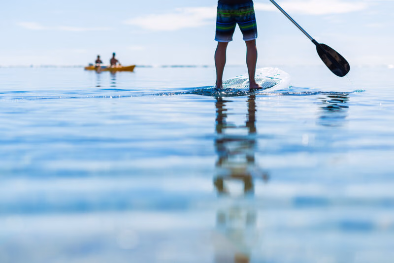 Person standing on a paddleboard in clear blue water during luxury adventure tours.