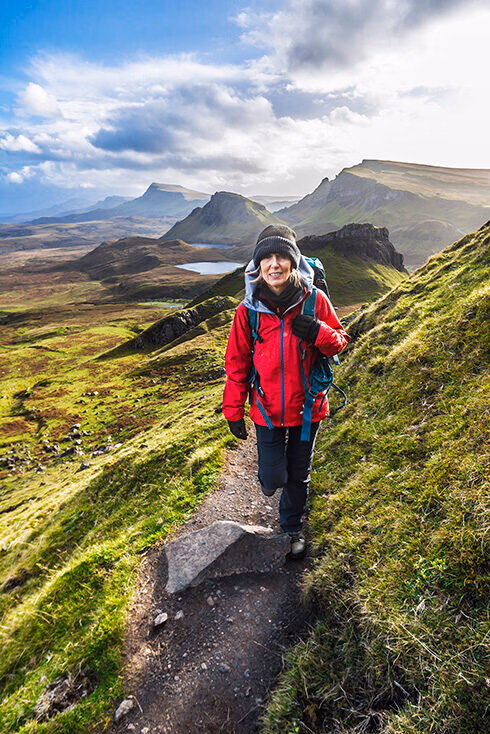 Hiker in a red jacket walking on a green mountain trail during luxury adventure tours.