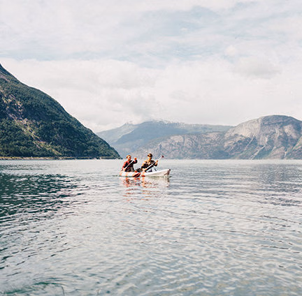 Two people kayaking on a tranquil lake with mountains in the background during luxury adventure holidays.