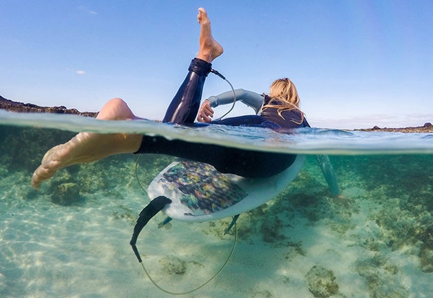 Over under photo of women paddling out on a surfboard
