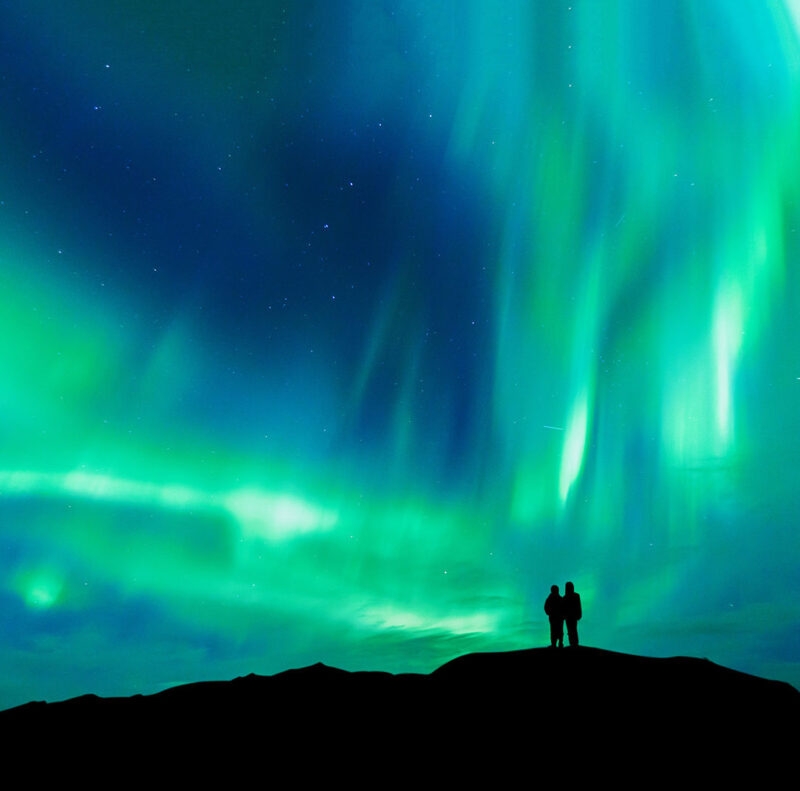 Aurora borealis with silhouette love romantic couple on the mountain.Honeymoon travel concept