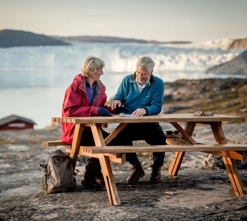 Two people sitting on a picnic bench in front of a large glacier