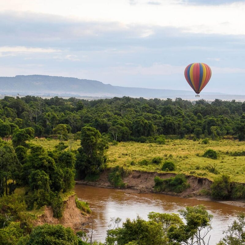 A rainbow striped hot a air balloon drifting over a river and forest