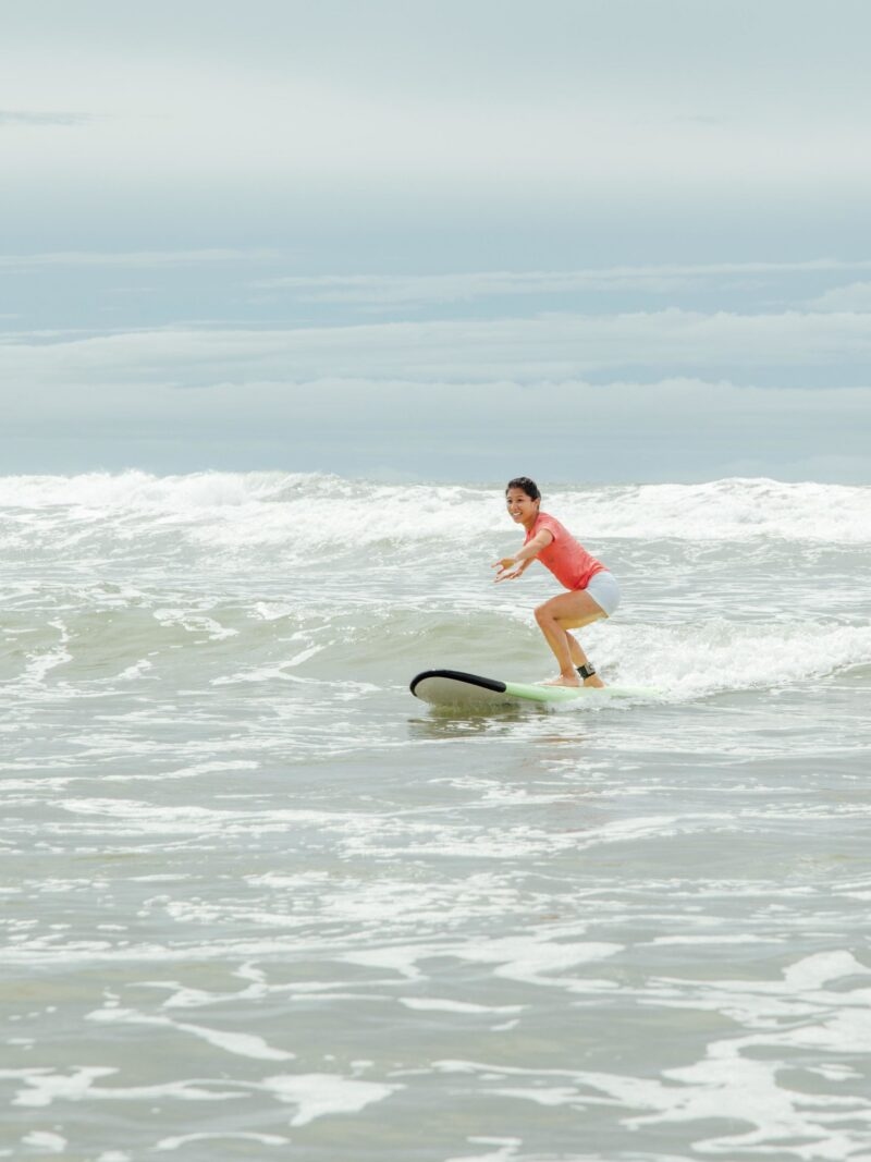 A person in an orange swim suit standing on a surf board on a wave during luxury Latin America family trips.