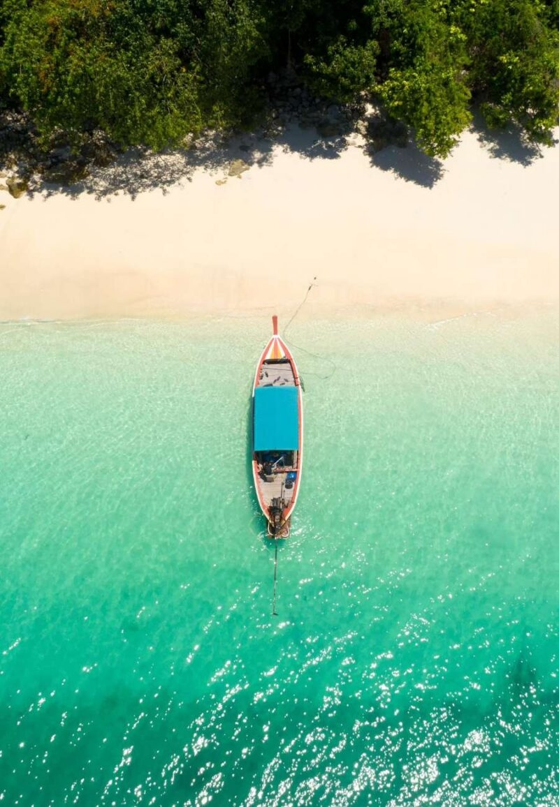 Overhead view of a boat in turquoise water for luxury Southeast Asia trips.